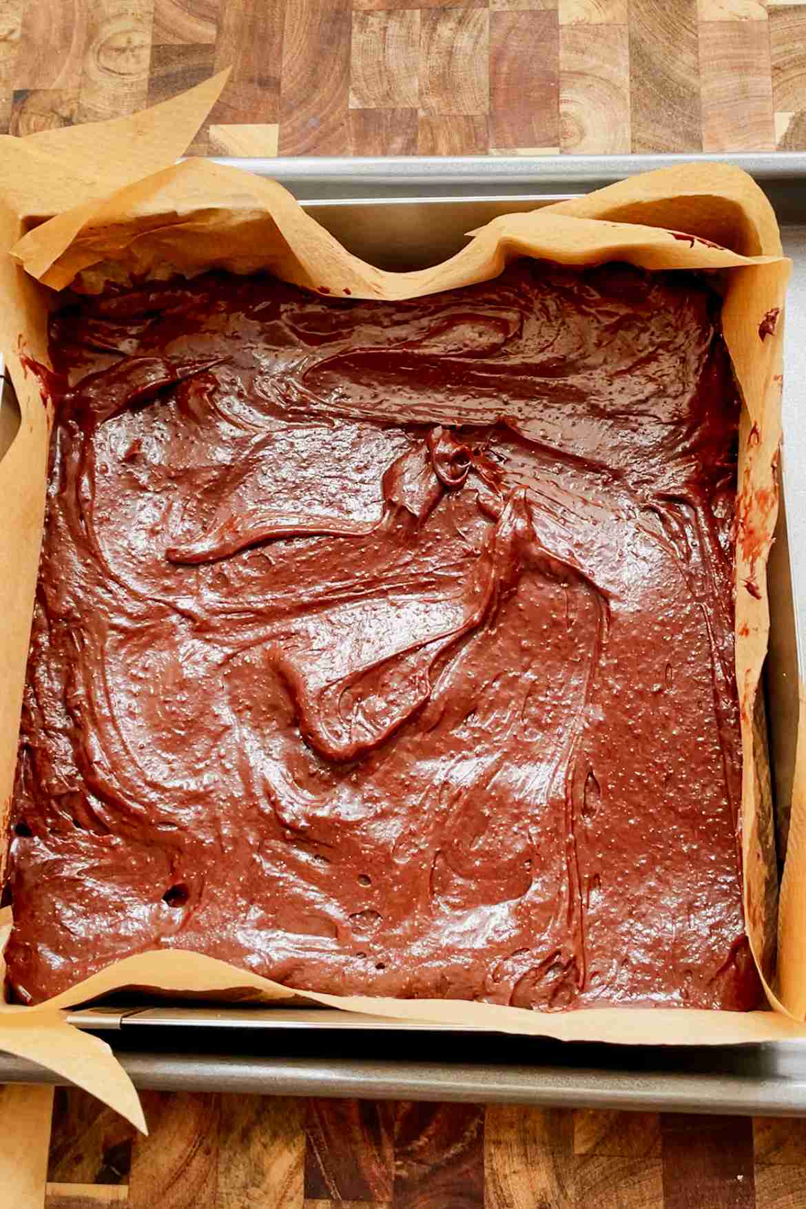 Fudgy sourdough brownie batter spread evenly in a parchment-lined square baking pan