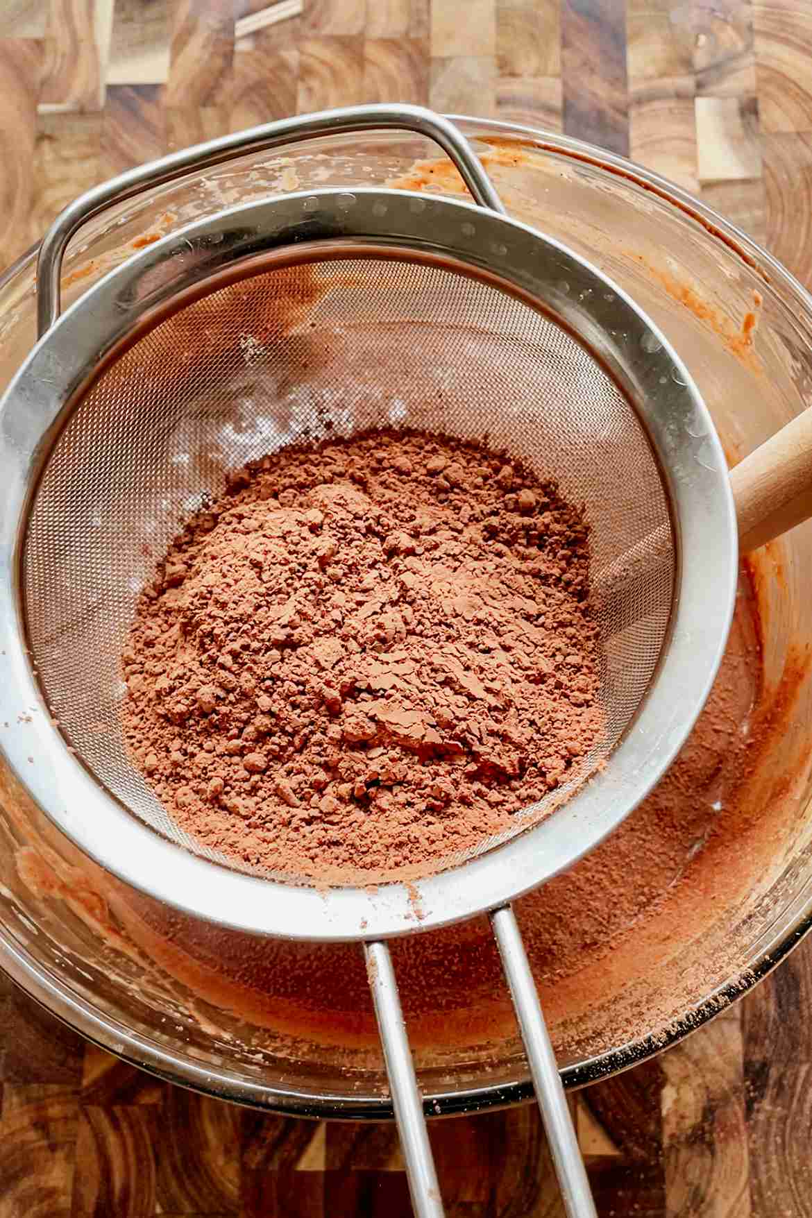 Cocoa powder being sifted through a strainer into sourdough brownie batter