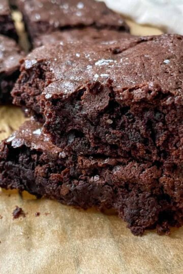 Stack of fudgy sourdough discard brownies with a shiny crackly top on a wooden board