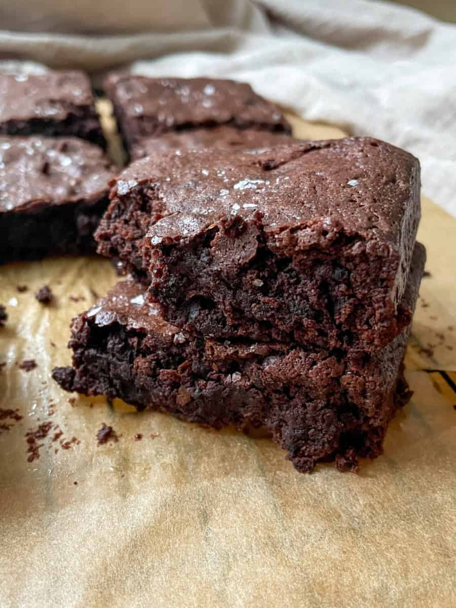 Stack of fudgy sourdough discard brownies with a shiny crackly top on a wooden board