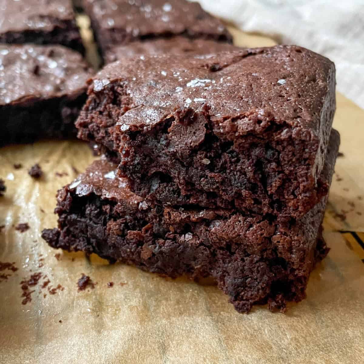 Stack of fudgy sourdough discard brownies with a shiny crackly top on a wooden board