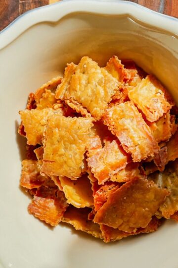 Stack of golden sourdough cheese crackers on a plate, crispy and studded with melted cheese.