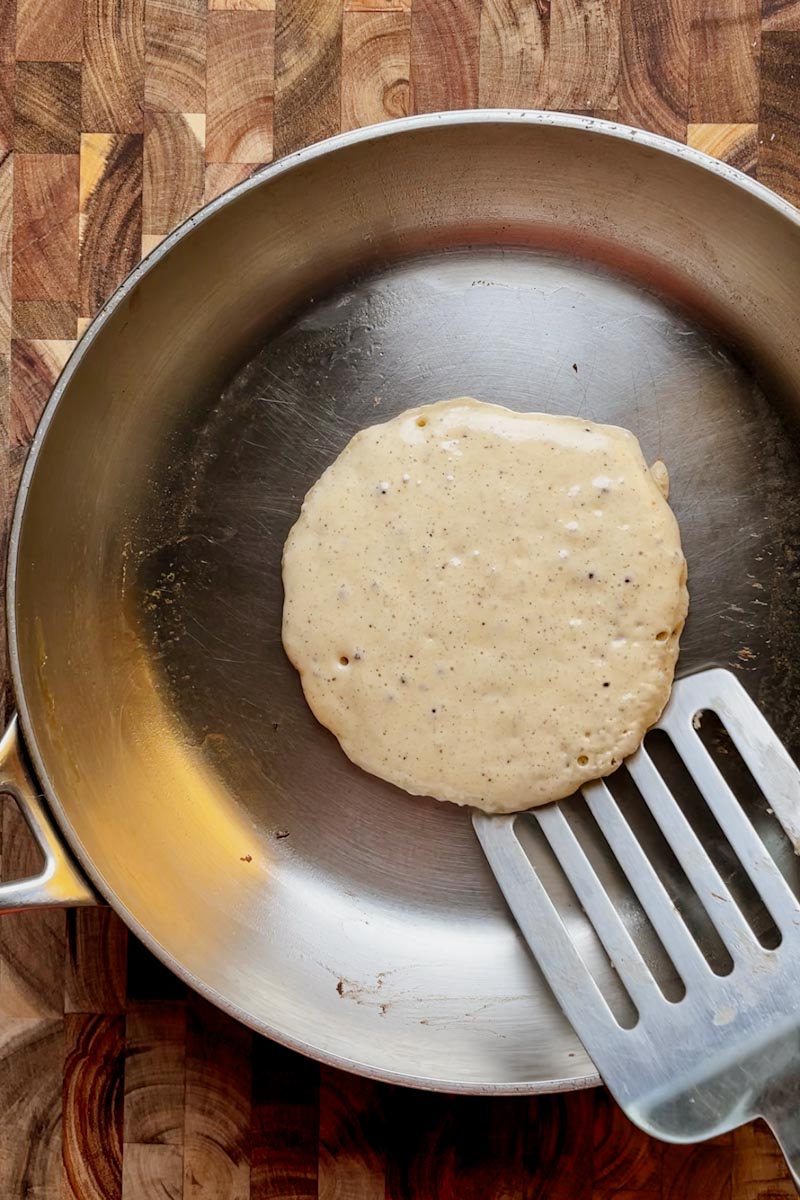 bubbles forming on sourdough pancake in pan before flipping