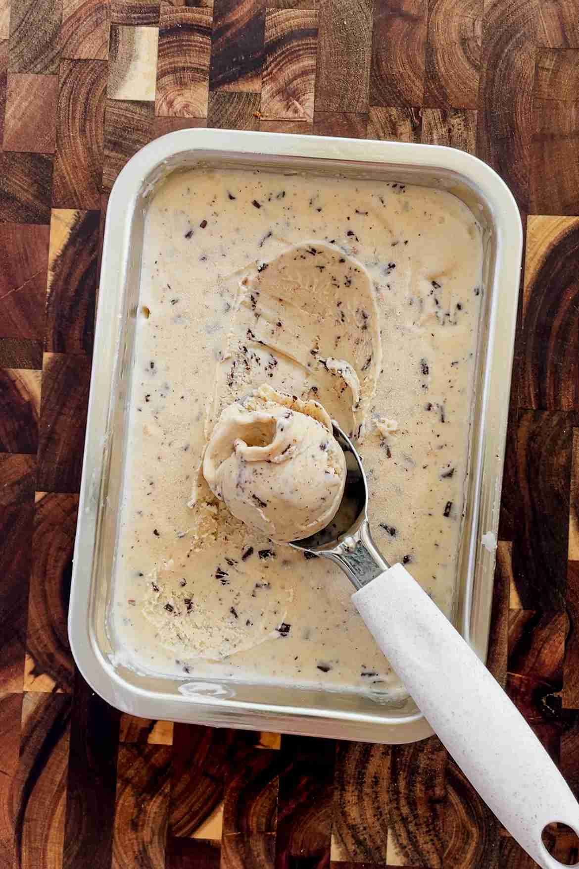 Scoops of hazelnut ice cream with dark chocolate shavings in a ceramic bowl, showing the creamy texture and flecks of chocolate.
