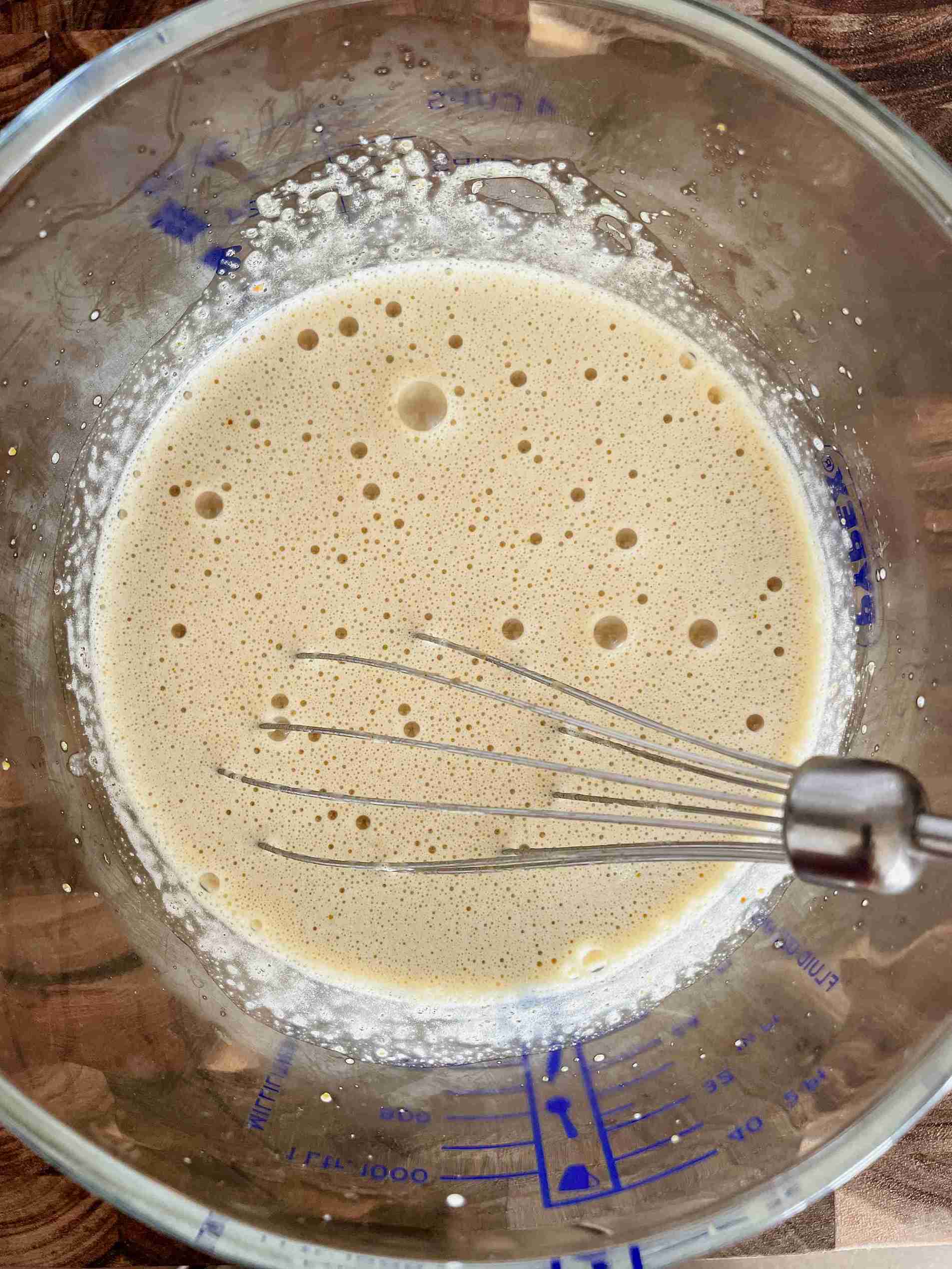 Warm pistachio milk being poured into egg yolks to temper them.