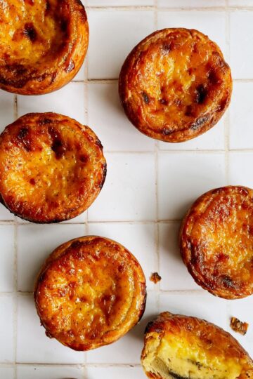 Portuguese puff pastry egg tarts on a wooden board with golden, slightly charred custard tops