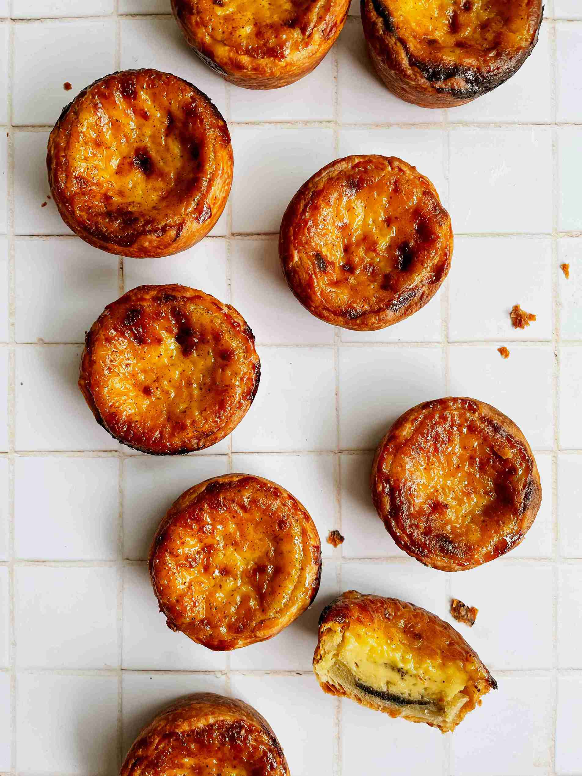 Portuguese puff pastry egg tarts on a wooden board with golden, slightly charred custard tops