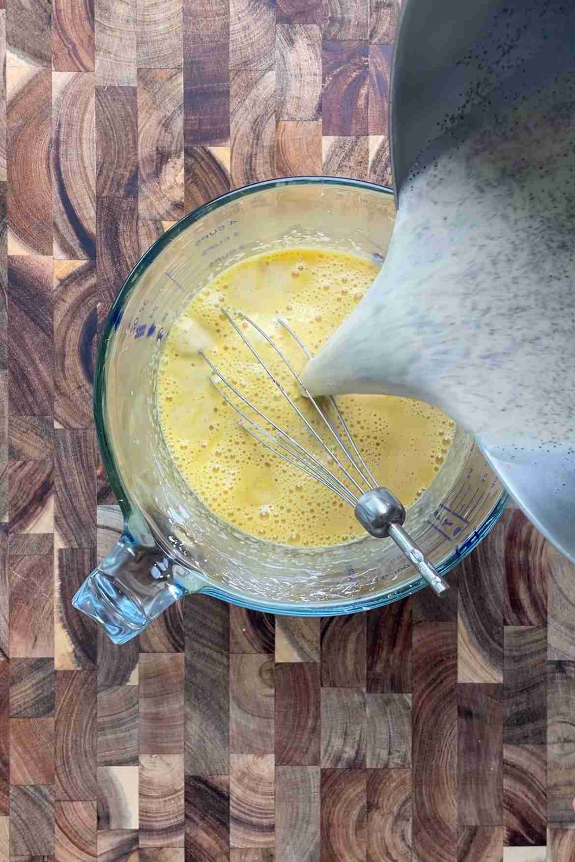 Slowly pouring warm cream and milk mixture into egg yolks while whisking to temper