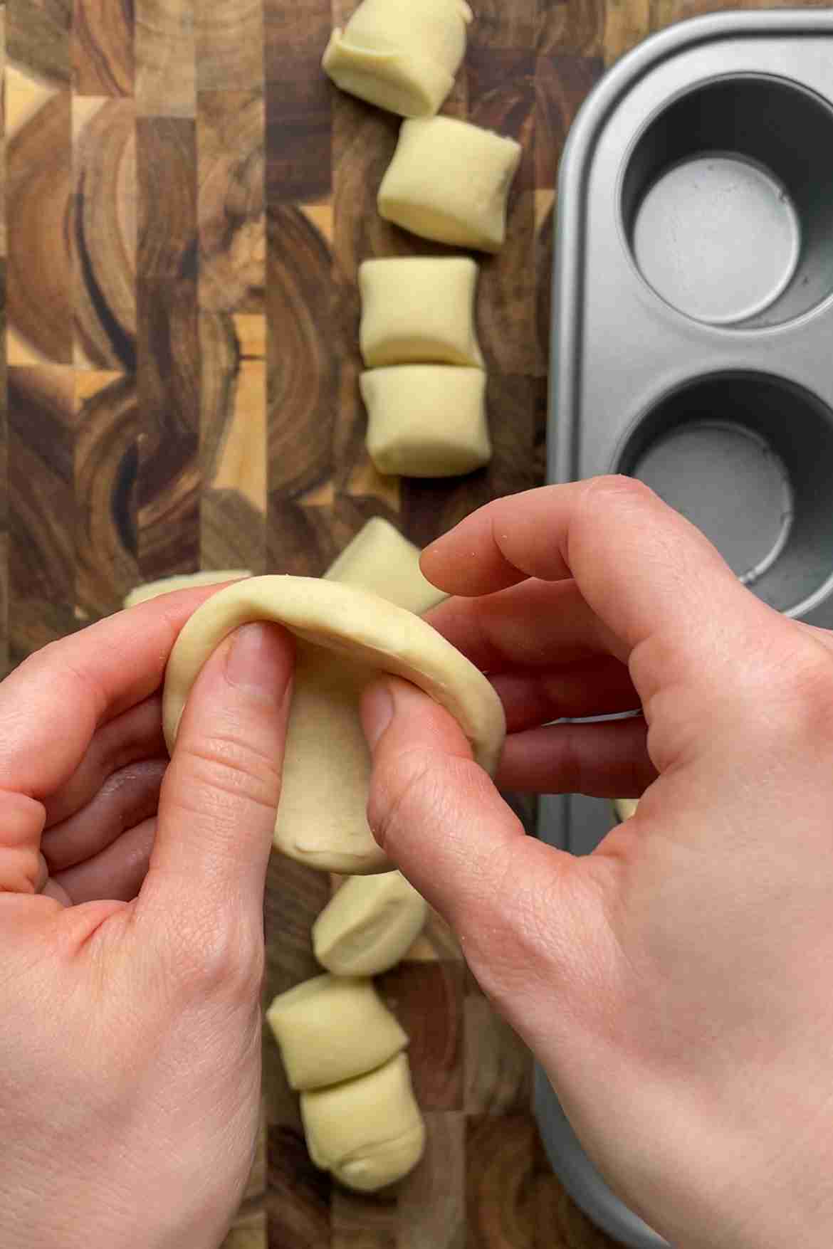 Hands pressing a puff pastry round into a muffin tin to form a custard tart shell