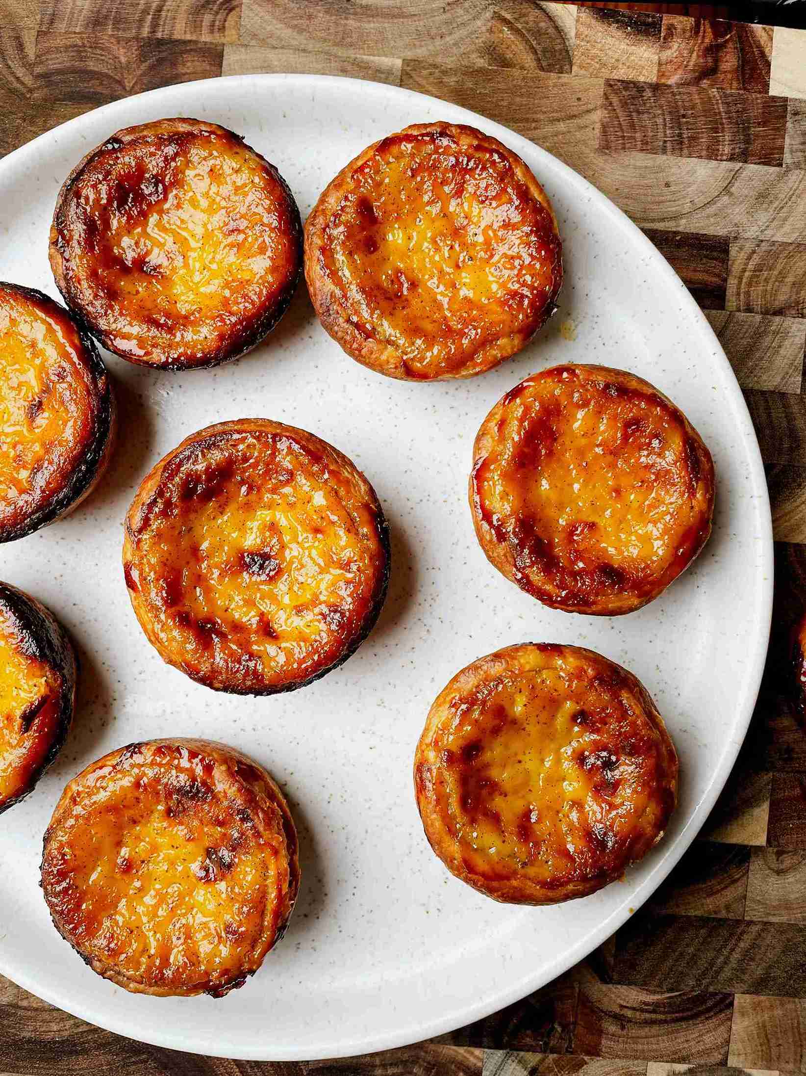 Freshly baked Portuguese puff pastry egg tarts in a muffin tin with golden flaky edges and charred custard tops