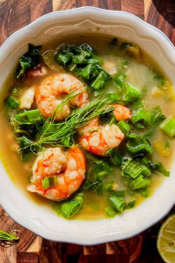 Bowl of swiss chard soup with fennel, shrimp, and calamari, topped with lemon and green onion.