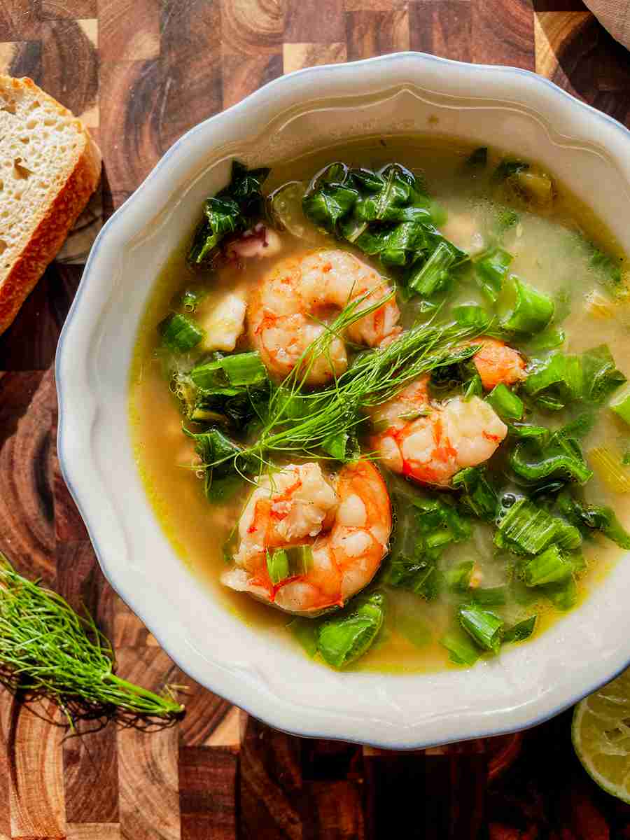 Bowl of swiss chard soup with fennel, shrimp, and calamari, topped with lemon and green onion.